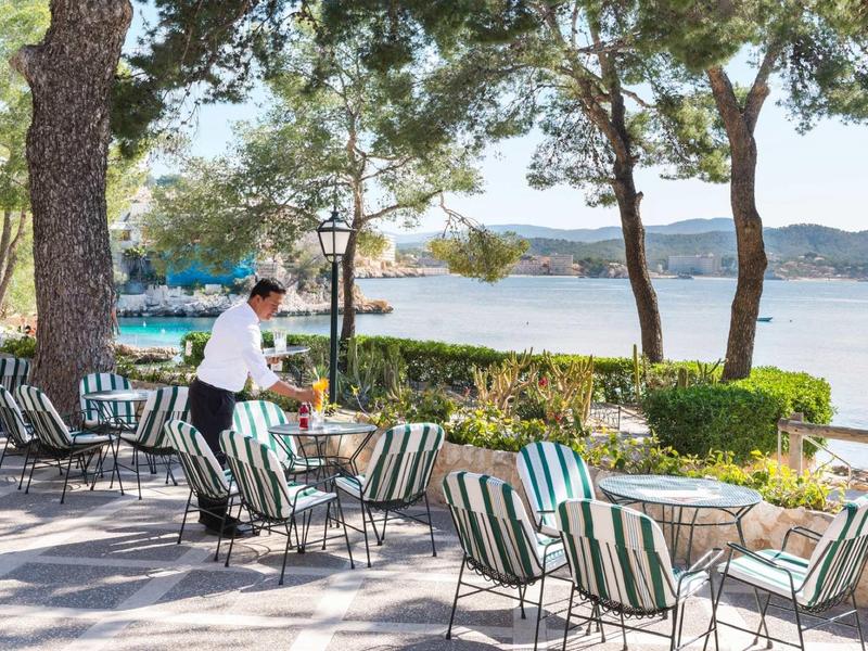 Kelner obsługujący stolik na tarasie z widokiem na wodę i drzewa.