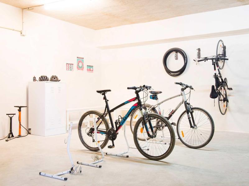 Pomieszczenie na rowery z dwoma rowerami, jednym wiszącym na ścianie oraz stojakami na rowery.