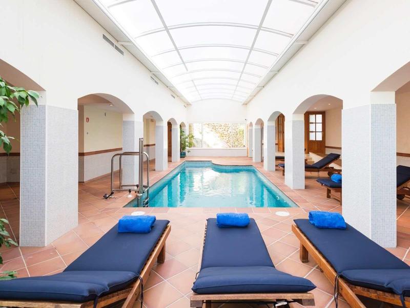 Basen kryty z niebieskimi leżakami i dużymi oknami, jasny sufit z naturalnym światłem.