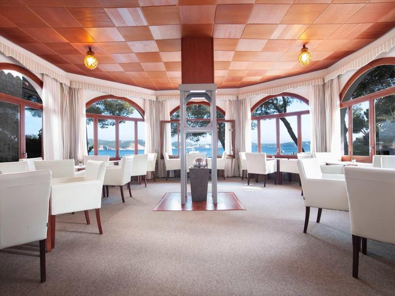 Jasno urządzone pomieszczenie z białymi fotelami i dużymi oknami z widokiem na jezioro.