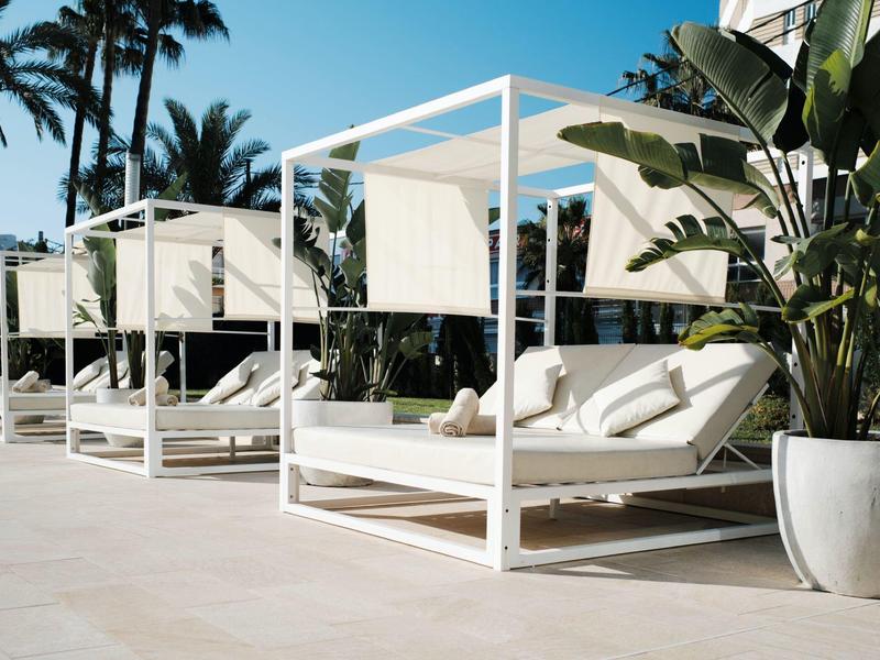 Białe parasole z wyściełanymi leżakami obok tropikalnych roślin i palm.
