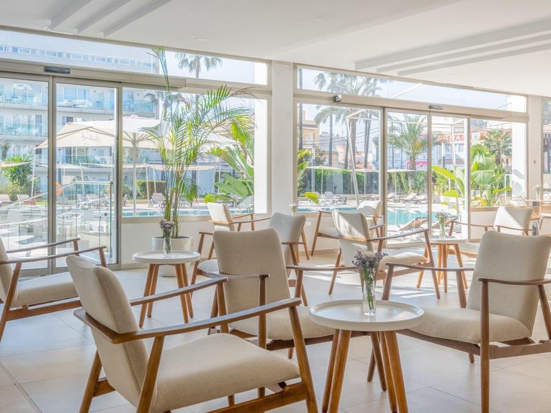 Nowoczesny hotelowy salon z wygodnymi fotelami i widokiem na taras i palmy.