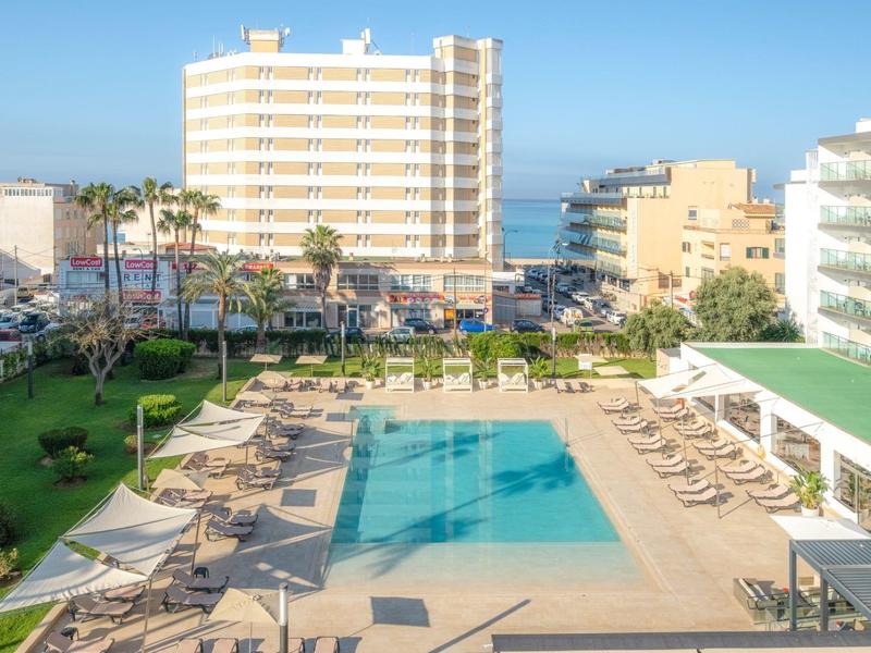 Basen hotelowy z leżakami, otoczony wielopiętrowymi budynkami i widokiem na morze w tle.