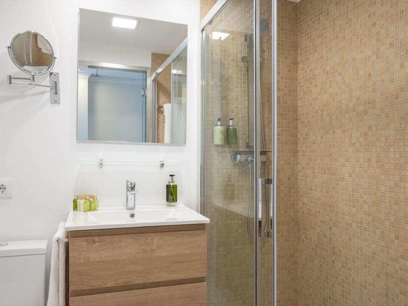 Nowoczesna łazienka z drewnianą szafką pod umywalką i prysznicem typu walk-in.