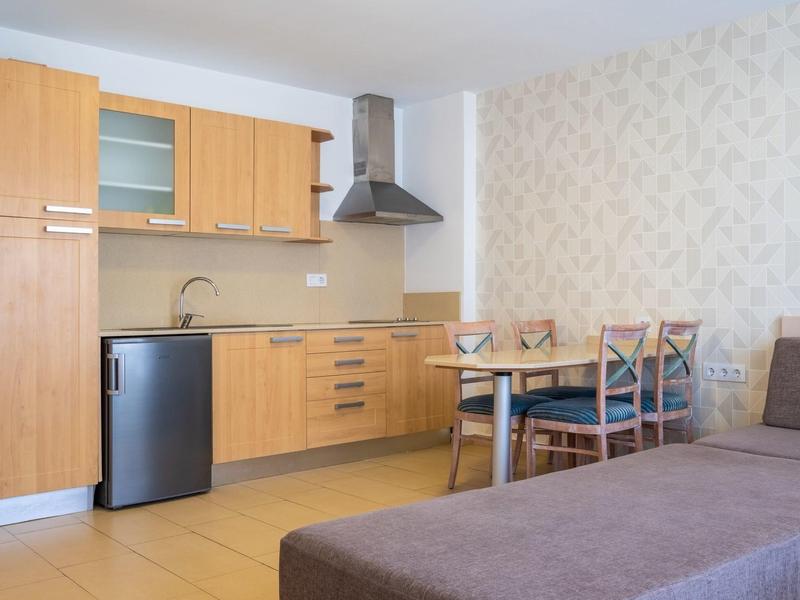 Kompaktowa kuchnia z drewnianymi szafkami, mini lodówką, stołem i sofą w części dziennej.