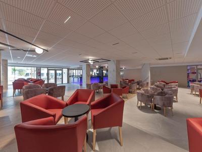 Geräumiger Hotel-Lounge-Bereich mit roten Sesseln und Tischen, hell und modern gestaltet.