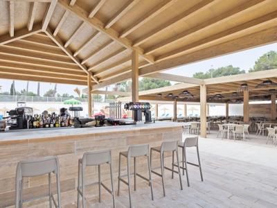 Moderner Außenbarbereich mit Holztheke und Hockern, umgeben von Sitzbereichen unter Holzdächern.