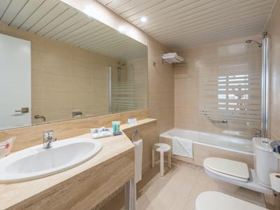 Moderní koupelna s umyvadlem, vanou, toaletou a velkými zrcadly v světlých odstínech.