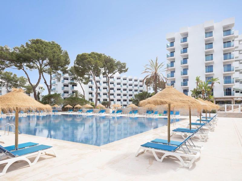 Moderní hotelový bazén s lehátky a slunečníky ze slámy pod modrou oblohou.