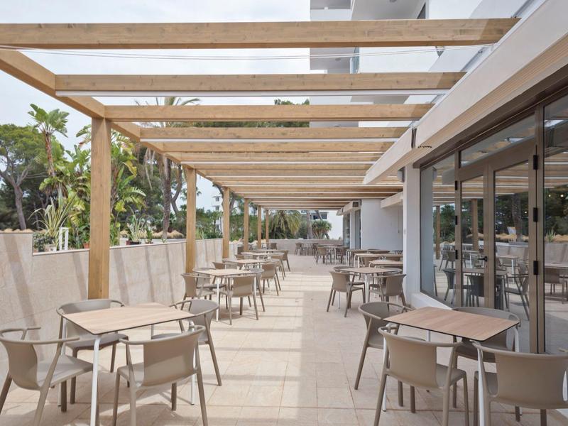 Terasa s dřevěnými trámy, několika stoly a židlemi vedle hotelové restaurace.