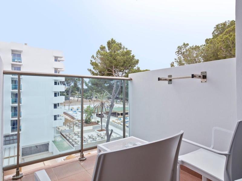 Balkon se židlemi a skleněným zábradlím s výhledem na hotely a stromy u moře