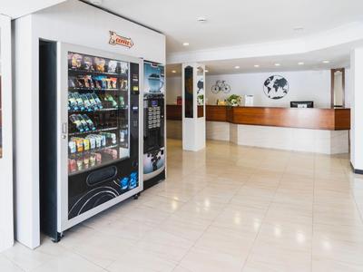 Moderní hotelová hala s automaty na občerstvení vlevo a recepcí v pozadí.