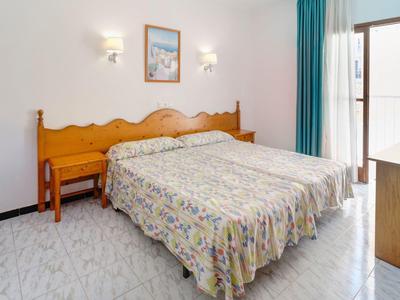 Helles Schlafzimmer mit zwei Einzelbetten, gemusterten Bettdecken, Fenstertür und blauen Vorhängen.