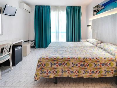 Moderní hotelový pokoj s manželskou postelí, psacím stolem a velkými závěsy u okna.