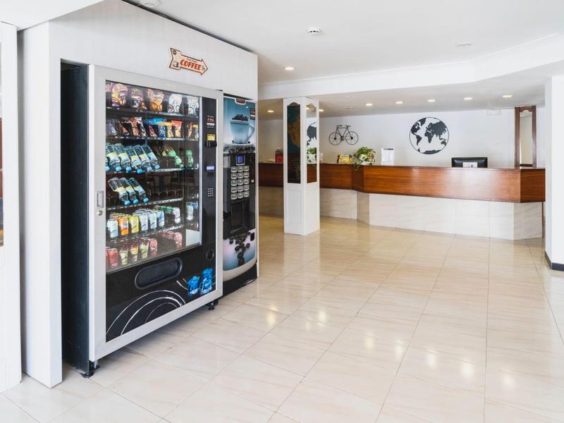 Heller Hotel-Lobby mit Snackautomat, weißem Boden, Holztresen und Weltkarte an der Wand.