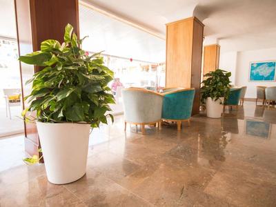 Jasny hol hotelowy z dużymi roślinami i wygodnymi fotelami.