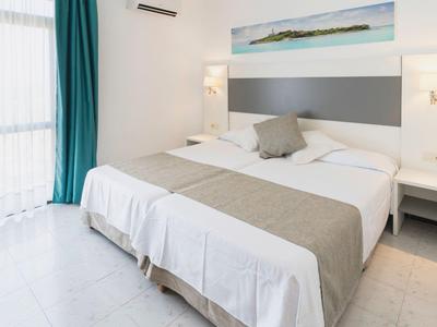 Bright hotel room with double bed, gray accents, and large window with blue curtain.