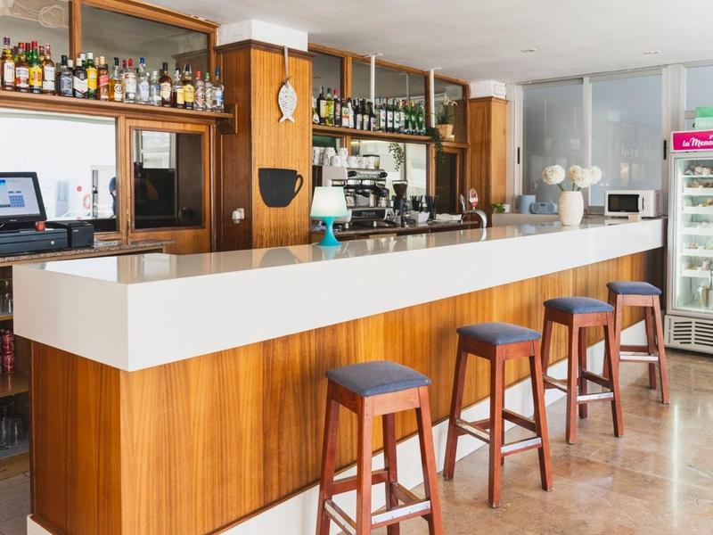 Modern hotel bar with four stools and illuminated beverage fridge in the background.