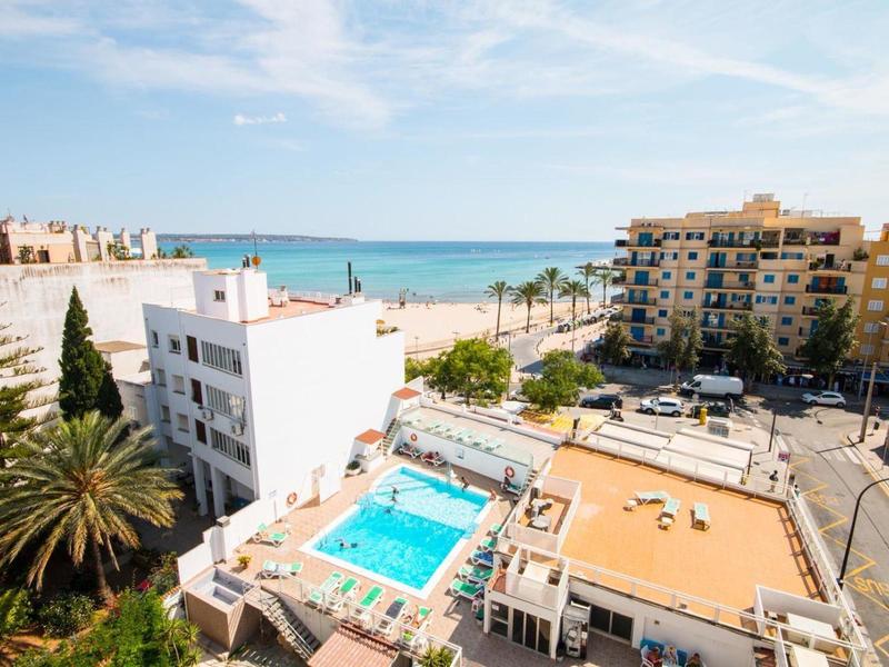 View of a hotel with pool near the beach and buildings in a coastal town.