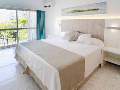 Bright hotel room with large double bed, nightstand, and balcony overlooking greenery.