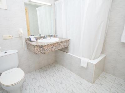 Bright bathroom with toilet, sink, wall mirror, and bathtub with shower curtain.