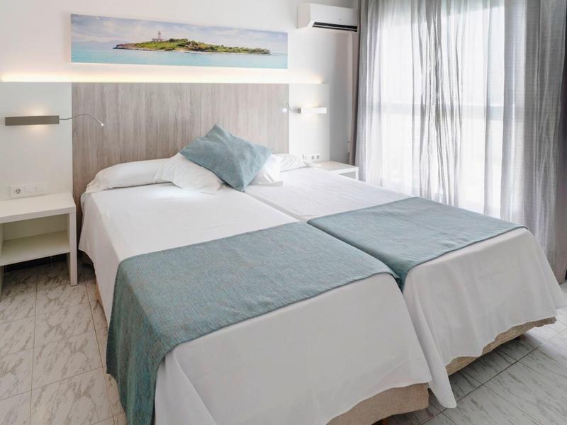 Bright hotel room with two single beds, gray curtains, and modern decor.