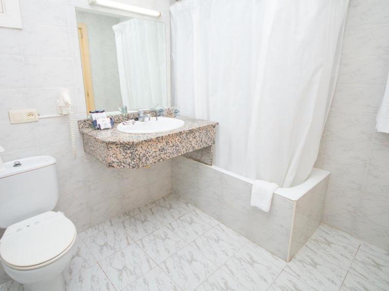 Bright bathroom with toilet, sink, wall mirror, and bathtub with shower curtain.