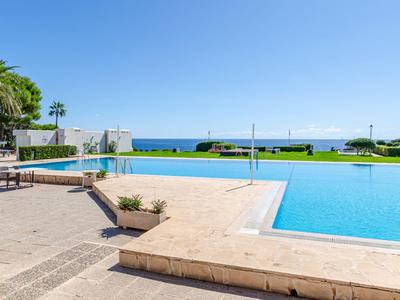 Großer Pool mit klarem Wasser, umgeben von Steinboden, Palmen und Meerblick bei klarem Himmel.