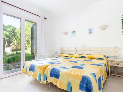 Helles Hotelzimmer mit großem Bett, buntem Bettwäsche und Blick auf Garten durch Glastür.