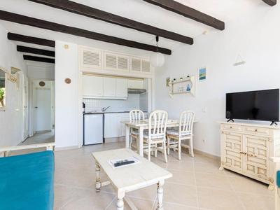Helles Wohnzimmer mit weißen Möbeln, Esstisch, TV und sichtbaren Deckenbalken.