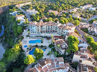 Luftaufnahme eines Hotels mit Pool, umgeben von Bäumen und Wohngebäuden in sonniger Gegend.