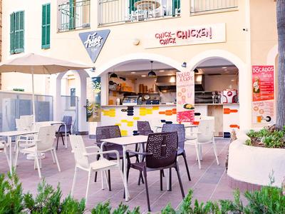 Außenbereich eines Cafés mit weißen Tischen und Stühlen in einer sonnigen Umgebung.
