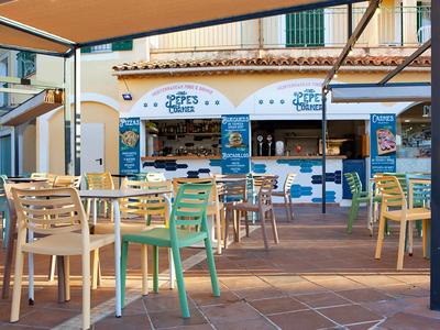 Freiluftrestaurant mit bunten Stühlen und Sonnenschutz in einem sonnigen Hotelbereich.