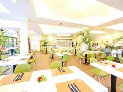 Helle, moderne Hotellounge mit weißen Tischen, grünen Stühlen und dekorativen Pflanzen.