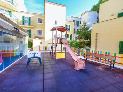 Bunter Kinderspielplatz mit Rutsche und Klettergerüst neben Hotelgebäuden bei klarem Himmel.