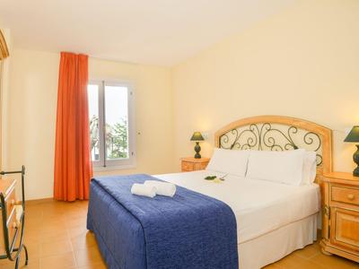 Helles Hotelzimmer mit Doppelbett, blauem Bettüberwurf und Holzmöbeln neben Balkon.