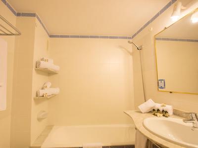 Hell beleuchtetes Badezimmer mit Badewanne, Spiegel und Waschbecken in Beige- und Weißtönen.