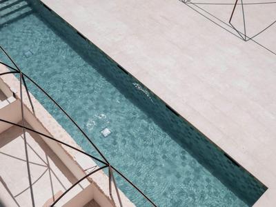 Schmaler, klarer Pool neben einer hellen, gefliesten Terrasse mit Metallgeländern.