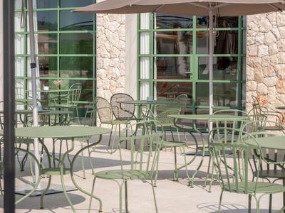 Leerer Außenbereich eines Cafés mit grünen Metalltischen und Stühlen vor einem Steingebäude.