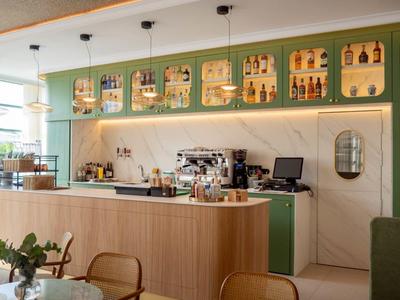Helles Café mit Holztheke, grünen Wänden und Regalen voller Weinflaschen und Gläser.