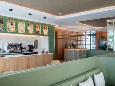 Moderne Hotel-Lounge mit grünem Sofa, Kaffeetheke und warmen Holzelementen.