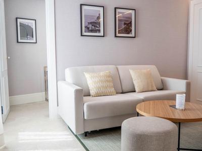 Helles Hotelzimmer mit grauem Sofa, Kissen und rundem Tisch vor weißem Hintergrund.