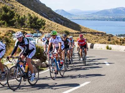 Gruppe von Radfahrern auf kurviger Straße mit Blick auf Meer und Hügel bei sonnigem Wetter
