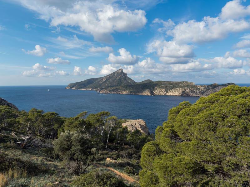 Küstenlandschaft mit blauem Meer, grün bewachsenen Hügeln und Inseln unter bewölktem Himmel.