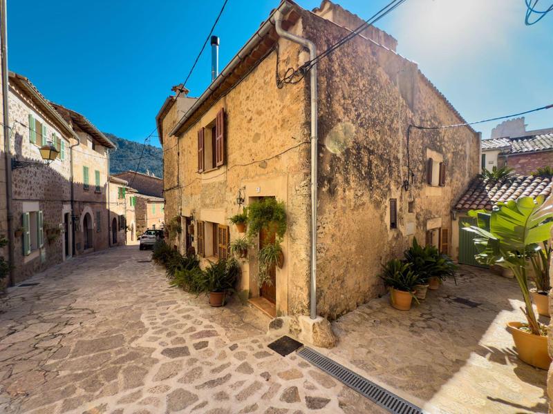 Eng gepflasterte Straße mit alten Sandsteinhäusern und Topfpflanzen unter blauem Himmel.