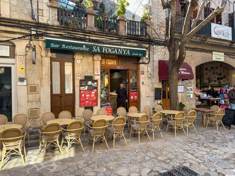 Außenansicht eines Restaurants mit vielen leeren Stühlen und Tischen auf gepflastertem Boden.