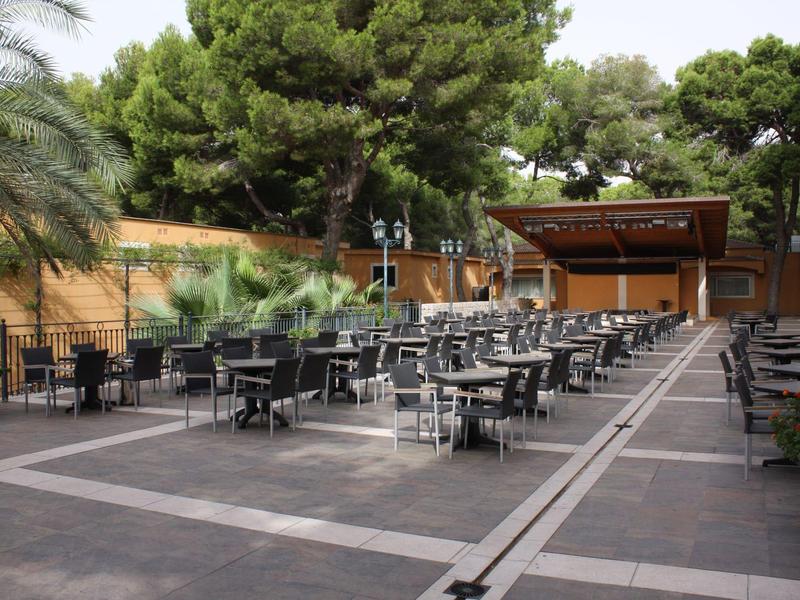 Große Terrasse mit vielen schwarzen Stühlen und Tischen, umgeben von grünen Bäumen und Holzwänden.