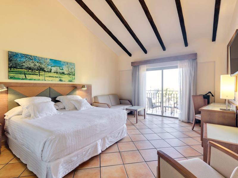 Helles Hotelzimmer mit zwei Betten, Balkon, Flachbildfernseher und Holzbalkendecke.