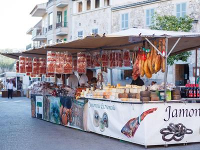 Marktstand mit verschiedener Wurst und Käse vor einem historischen Gebäude in sonniger Umgebung