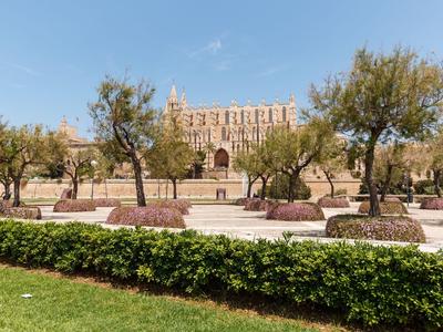 Historisches Gebäude mit großem Eingangsbereich, umgeben von Bäumen und gepflegten Gärten.
